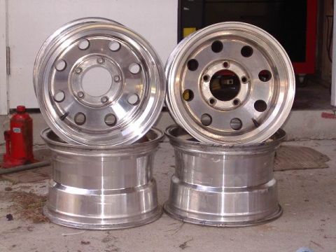 1985 Ford Bronco - A pair of aluminum wheels are stacked on top of another pair of aluminum wheels, with a red jack nearby.
