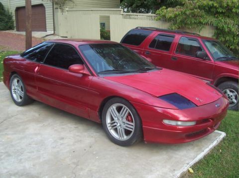 1995 Ford Probe - A red 1995 Ford Probe coupe is parked next to a red SUV.