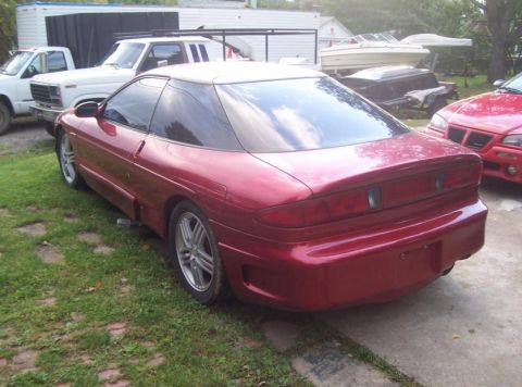 1995 Ford Probe - A red coupe is parked in a grassy area next to a white truck and other vehicles.