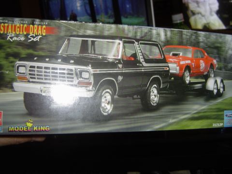1989 Ford Bronco - A black Ford Bronco tows a red drag car on a trailer, depicted on a model kit box.