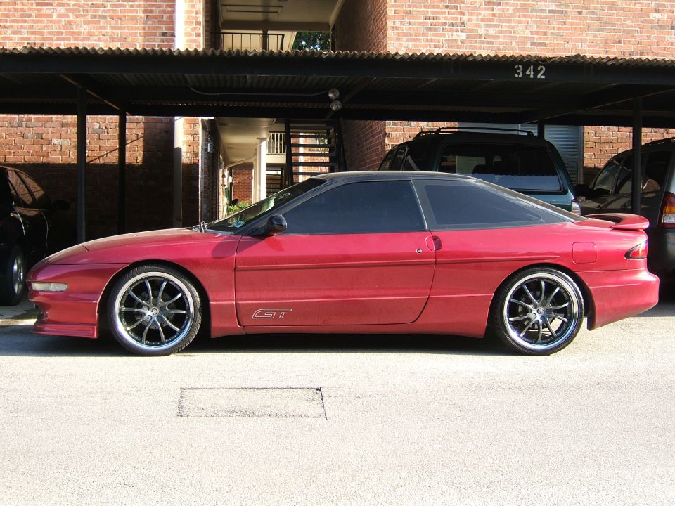 Lowered red Ford Probe GT in profile on dark multi-spoke wheels at a carport