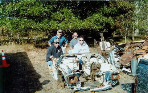 1997 Jeep TJ - Four men pose with a heavily damaged car chassis in an outdoor junkyard setting.