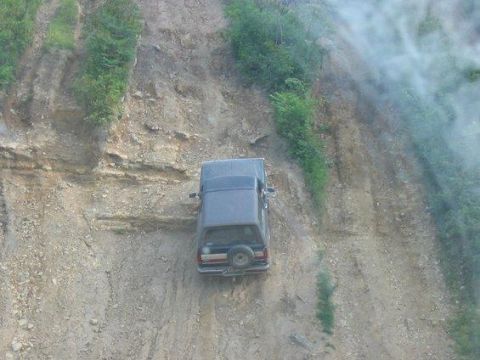 1988 Ford Bronco - SUV navigates a precarious dirt slope with vegetation on the side.