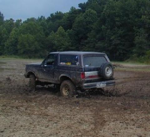 1988 Ford Bronco - Muddy 1988 Ford Bronco navigating through a muddy field with trees in the background.