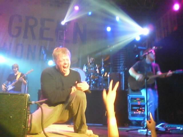 Band performing on stage with lights and a banner that says GREEN