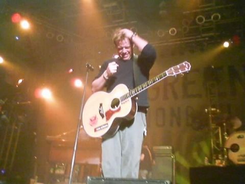 1989 Ford Bronco - A musician performs on stage with an acoustic guitar, bathed in warm stage lighting.