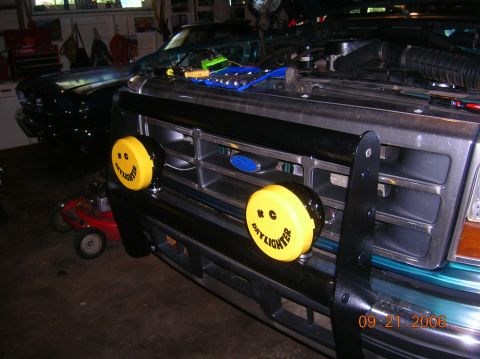 1996 Ford Bronco - 1996 Ford Bronco front end yellow smiley face off-road lights and a black grille guard. Another vehicle is visible in the background.
