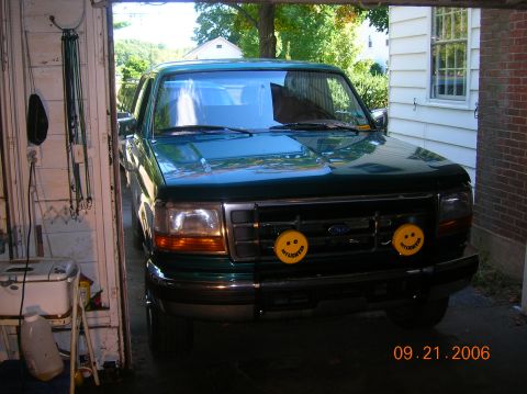 1996 Ford Bronco - A green Ford truck is parked in a garage, with yellow smiley face lights mounted on the front grille.