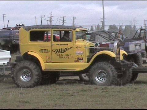 1985 Ford Bronco - This heavily modified sedan, adorned with Miller Genuine Draft branding, sits on large off-road tires, with other vehicles visible in the b…