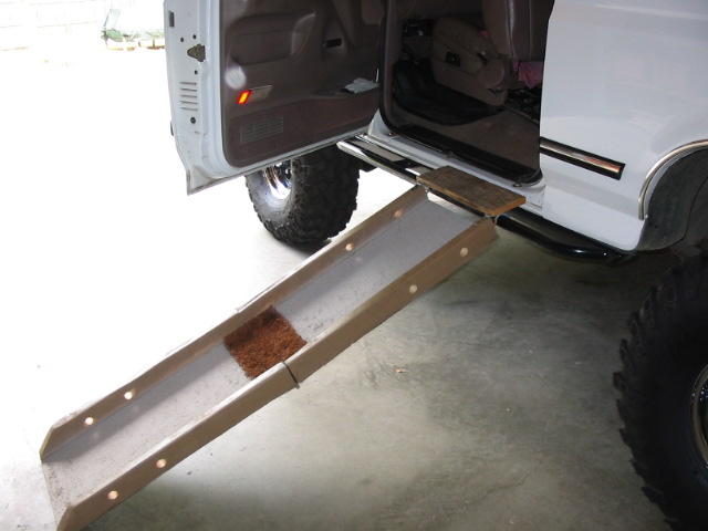 White lifted Bronco in garage with door open and wooden ramp against the running board.