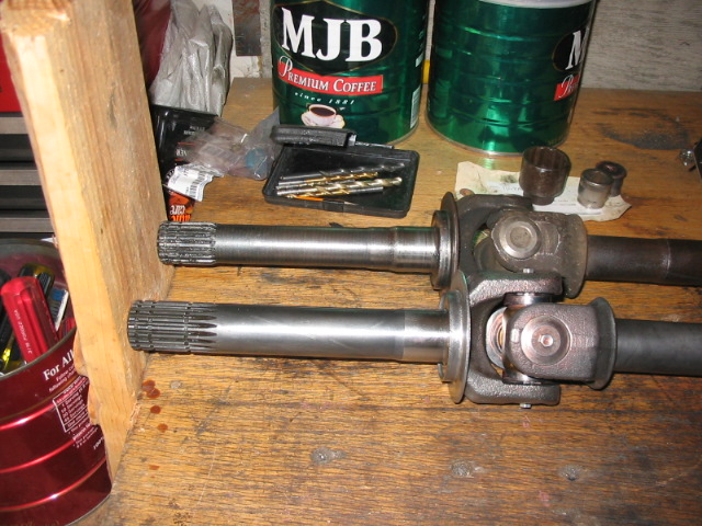 Two splined axle shafts with U-joints on a wooden workbench near MJB coffee cans and tools.