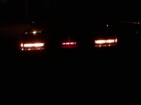 1985 Ford Crown Victoria LTD - The rear lights of three vehicles are visible in the dark.
