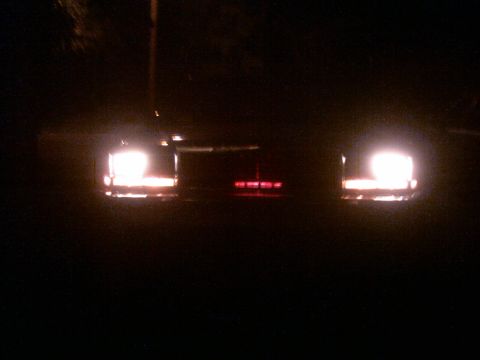 1985 Ford Crown Victoria LTD - The taillights and a central red light bar are visible on the rear of a dark vehicle at night.