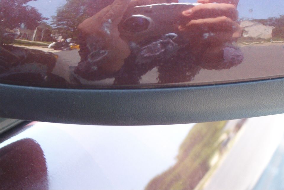 Close-up of a rearview mirror reflecting the photographer holding a camera and a street scene