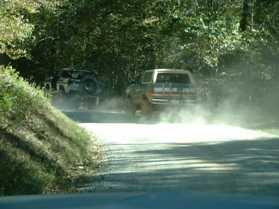 Two SUVs kicking up dust on a dirt road, one in front and one behind