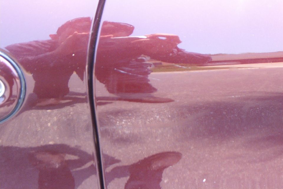 Close-up of glossy dark maroon car body panel and door seam with photographer reflected in the paint