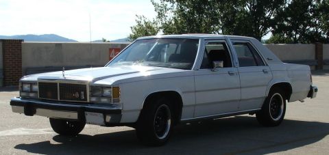 1985 Ford Crown Victoria LTD - This white sedan is parked on a rooftop with mountains visible in the distance.