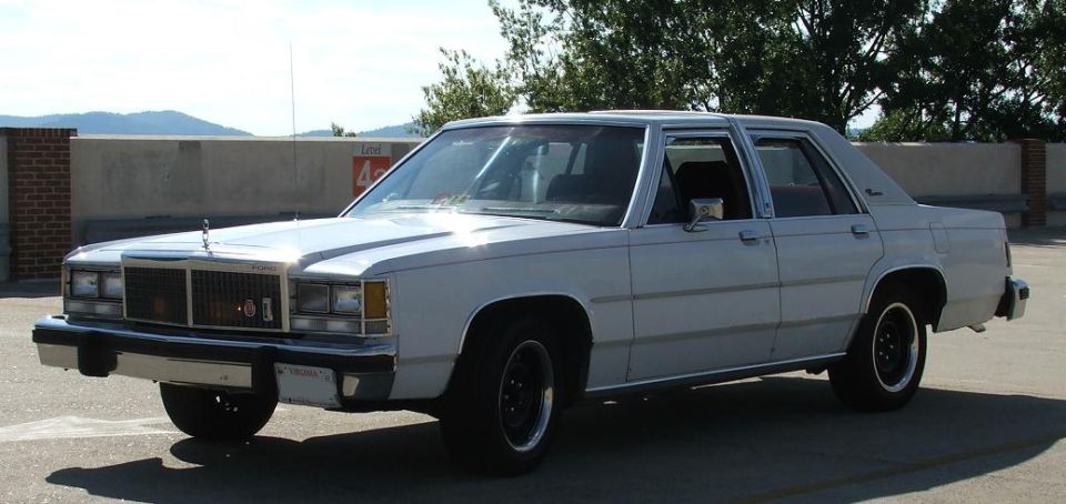 White sedan parked on a rooftop, mountains in background. Has a chrome grille and hood ornament