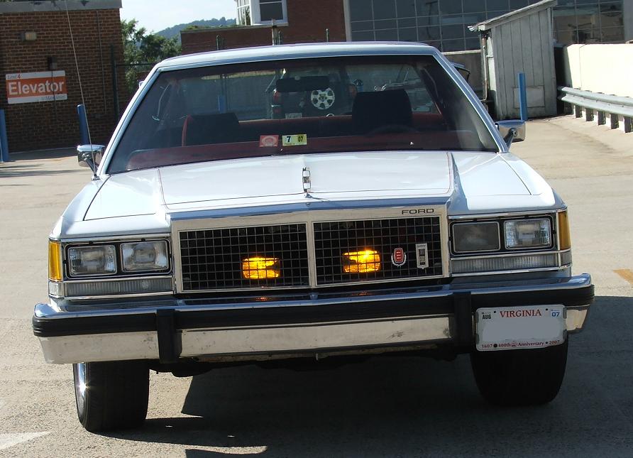 Silver 1980s Ford sedan, front view, with chrome grille and amber turn signals. Virginia license plate reads 'VIRGINIA 07'