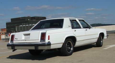 1985 Ford Crown Victoria LTD - The rear of a white sedan is shown parked on a rooftop with a building in the background.