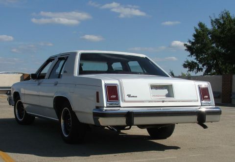 1985 Ford Crown Victoria LTD - Rear view of a white 1985 Ford Crown Victoria LTD sedan, showing its distinctive taillights and chrome bumper.
