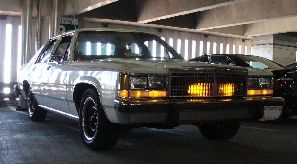 White 1980s Ford sedan parked in a garage, front view. Another car is visible behind it