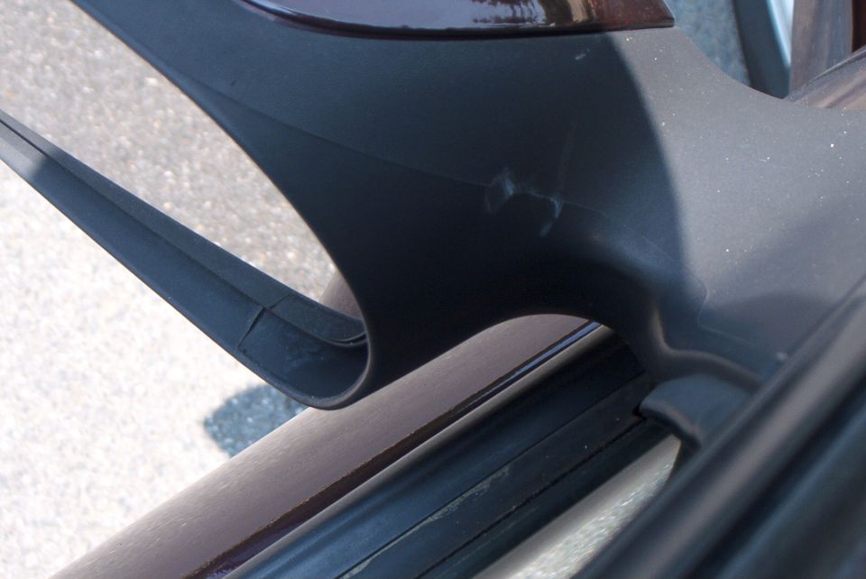 Close-up of black side mirror housing base with minor scuffs, window sill weatherstrip visible below