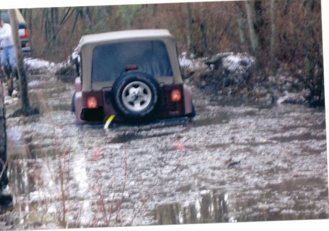 1997 Jeep TJ - A Jeep Wrangler navigates a wet, wooded trail with snow on the ground.