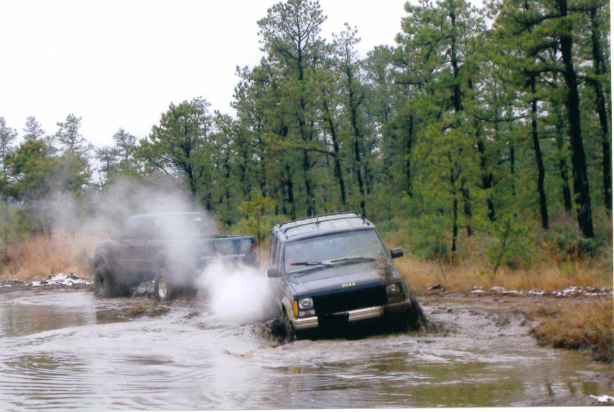 Jeep Cherokee XJ driving through mud and water with another vehicle behind it