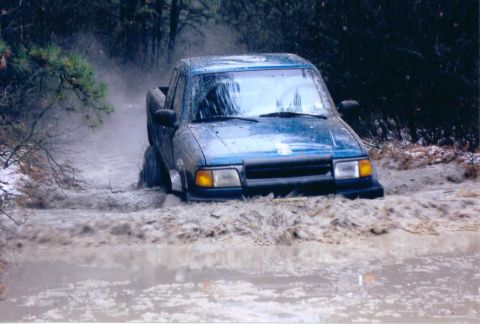 1997 Jeep TJ - Pickup truck navigating a muddy trail, kicking up water and mud.