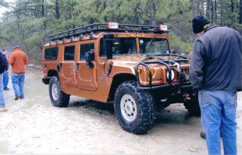 1997 Jeep TJ - A group of people stand around a Hummer H1 parked on a dirt road in a wooded area.