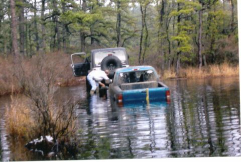 1997 Jeep TJ - Two off-road vehicles are stuck in the water, with one person attempting to assist.