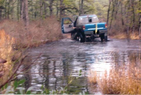 1997 Jeep TJ - Pickup truck navigates through water in a wooded off-road environment.
