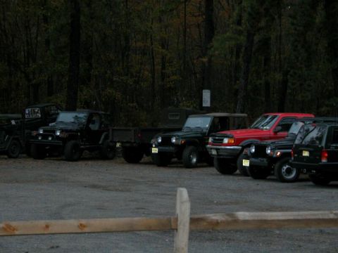 1997 Jeep TJ - Multiple Jeeps and a red SUV are parked in a lot, with trees in the background.