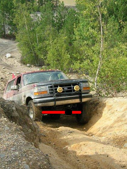 1995 Ford Bronco - A red 1990s Ford full-size truck or Bronco with a brush guard and yellow-covered auxiliary lights descends into a deep dirt trench while wh…