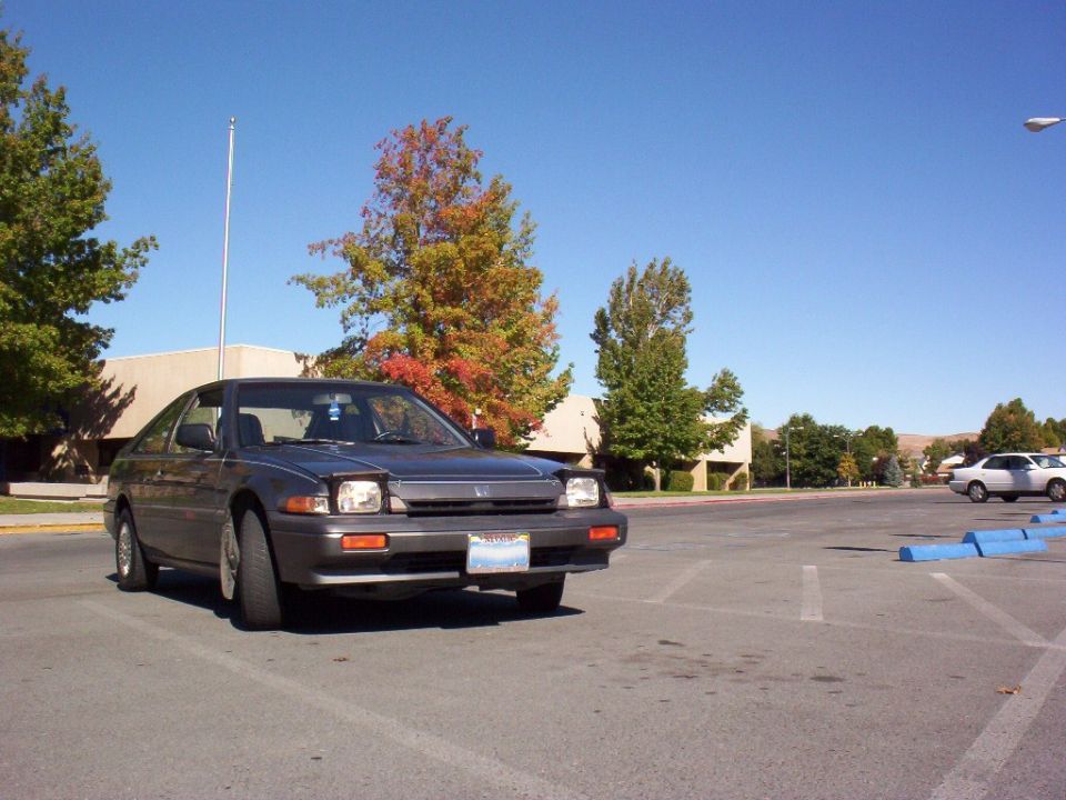 Gray Honda Accord coupe parked in lot, front 3/4 view, Nevada plate, autumn trees behind.
