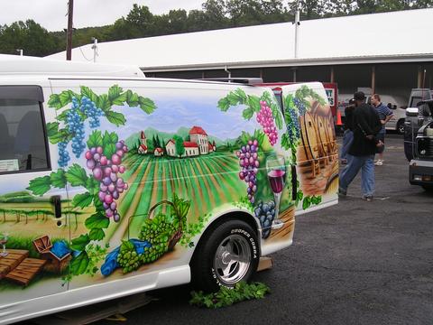 1978 Ford Mustang II - A van features a detailed mural depicting a vineyard scene with grapes and wine barrels, parked outdoors with other vehicles visible.