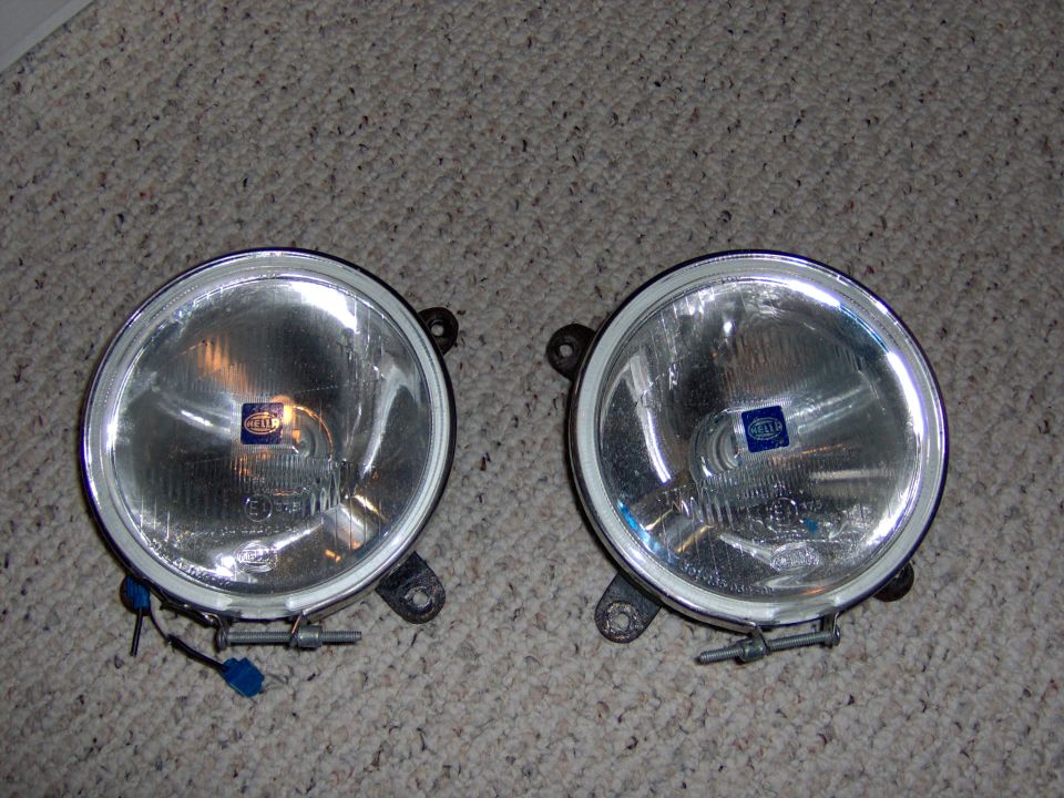 Two round Hella fog lamps with brackets and wiring laid on carpet
