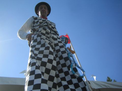 1990 Ford Bronco - stilt walker dressed in a black-and-white checkered costume and top hat towers against a clear blue sky.