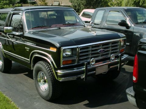 1984 Ford Bronco - A black Ford Bronco is parked in a driveway with other vehicles visible in the background.