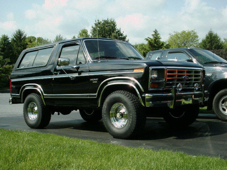 Dark green square-body Ford Bronco with brush guard and oversized tires