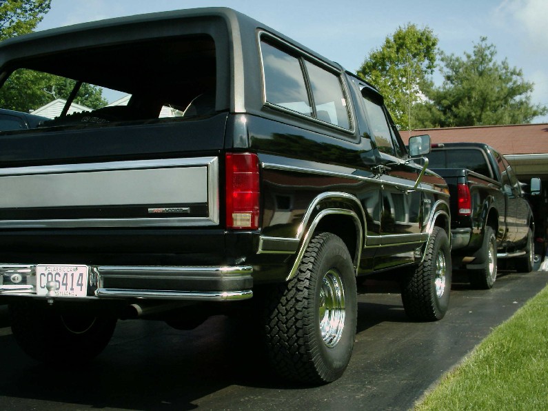 Black SUV rear view, chrome bumper, license plate CPS414, with a black pickup truck behind it