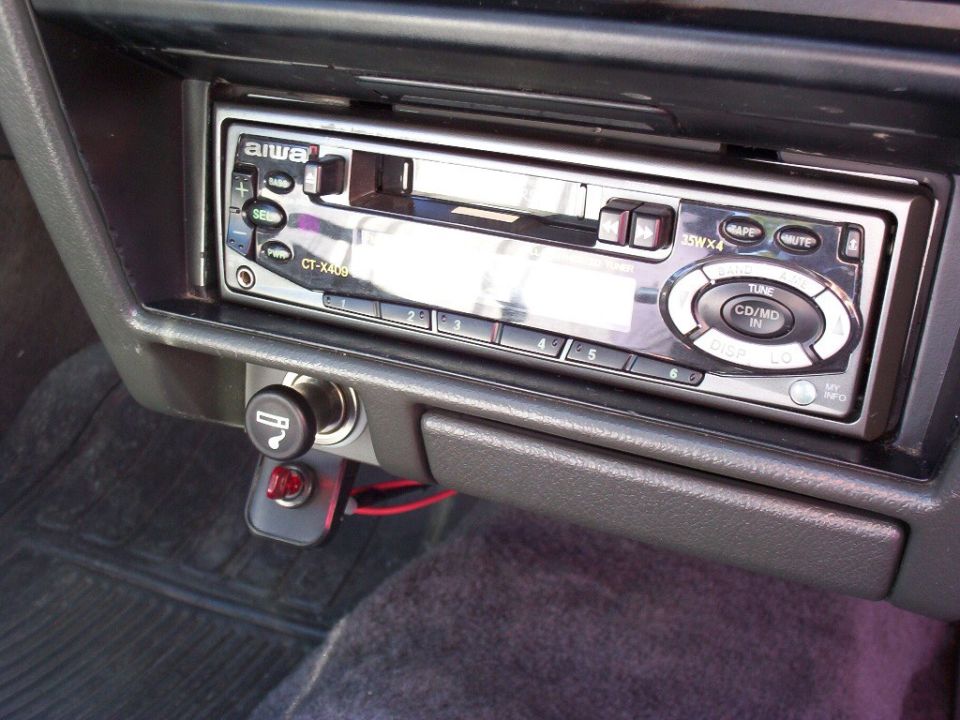 Aiwa CT-X409 cassette stereo in black dash of a car, with lighter socket and added red toggle switch below