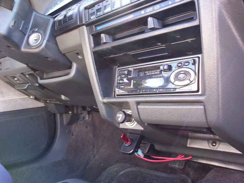 Gray car dash with aftermarket cassette stereo and added toggle switch with red wiring below