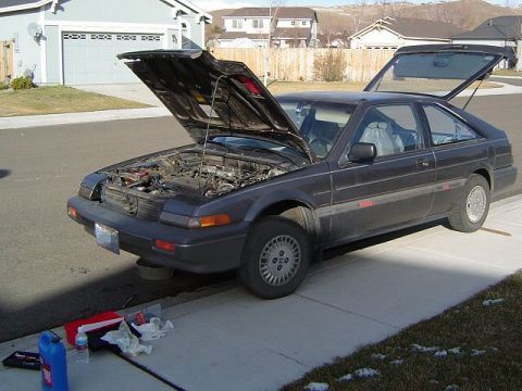 1986 Honda Accord - A dark gray 1986 Honda Accord coupe is parked on a residential street with its hood and trunk open, suggesting maintenance work.