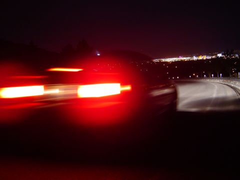1986 Honda Accord - Motion blur captures the red taillights of a car driving at night, with a city visible in the distance.
