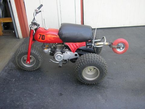 1900 Honda Big Red - A red three-wheeled ATV with a black seat and flame decals is parked on a dark surface.