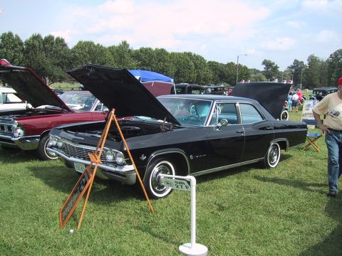 1968 Shelby GT500 - A black 1965 Chevrolet Impala is displayed at a car show with its hood open, alongside other vehicles.