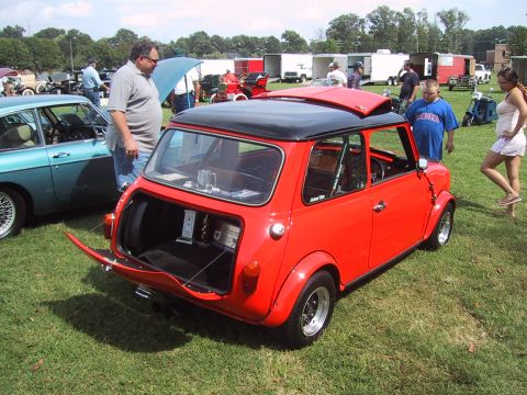 1968 Shelby GT500 - A red Mini Cooper is displayed with its trunk open at a car show, alongside other vehicles and attendees.