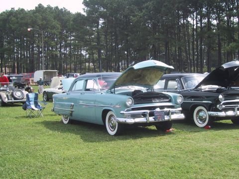 1968 Shelby GT500 - A light blue sedan from 1954 is displayed with its hood open at an outdoor car show.